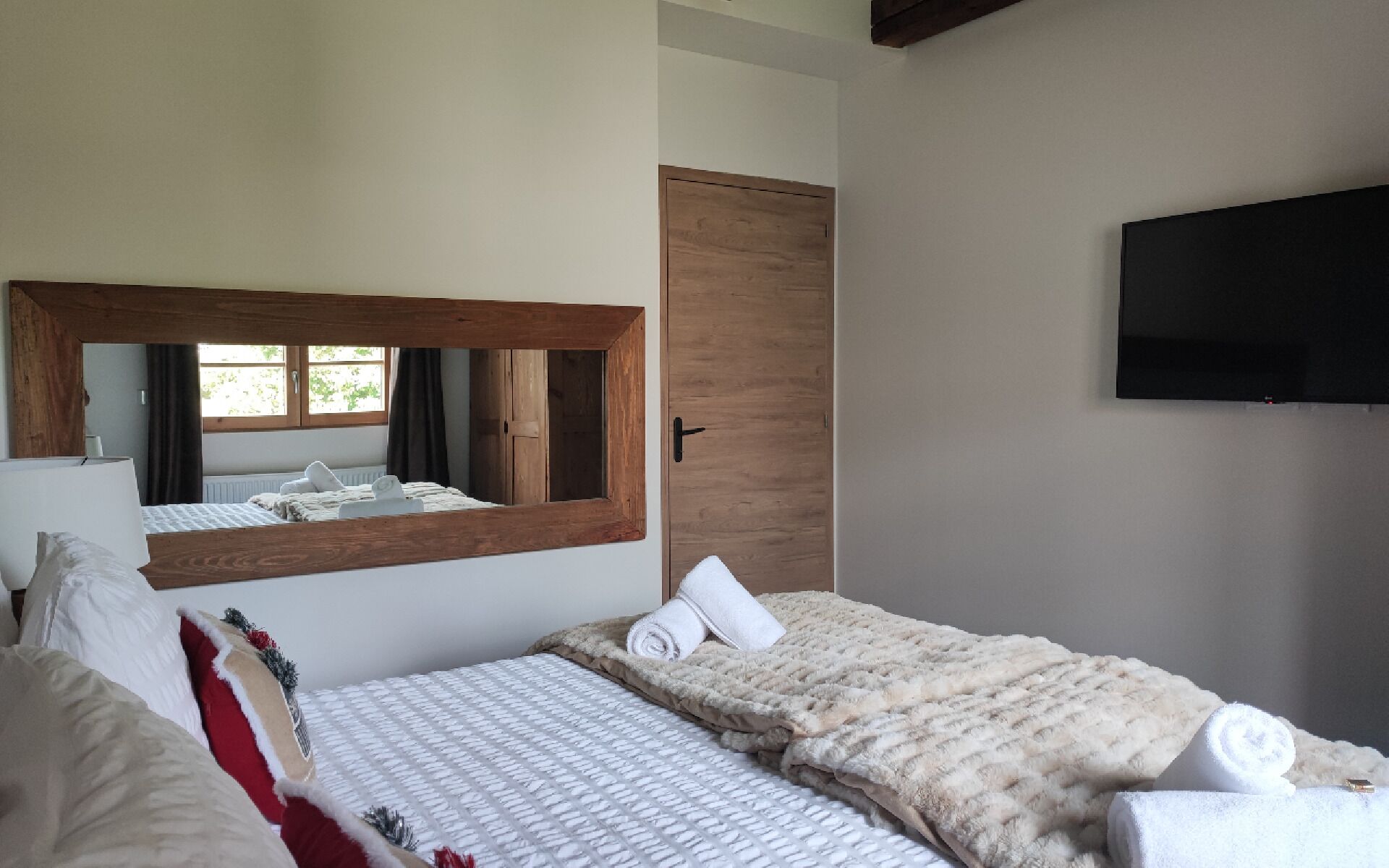 A hotel room with two beds, a large mirror, a wooden door, and a flat-screen TV mounted on the wall.