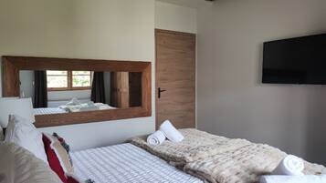 A hotel room with two beds, a large mirror, a wooden door, and a flat-screen TV mounted on the wall.
