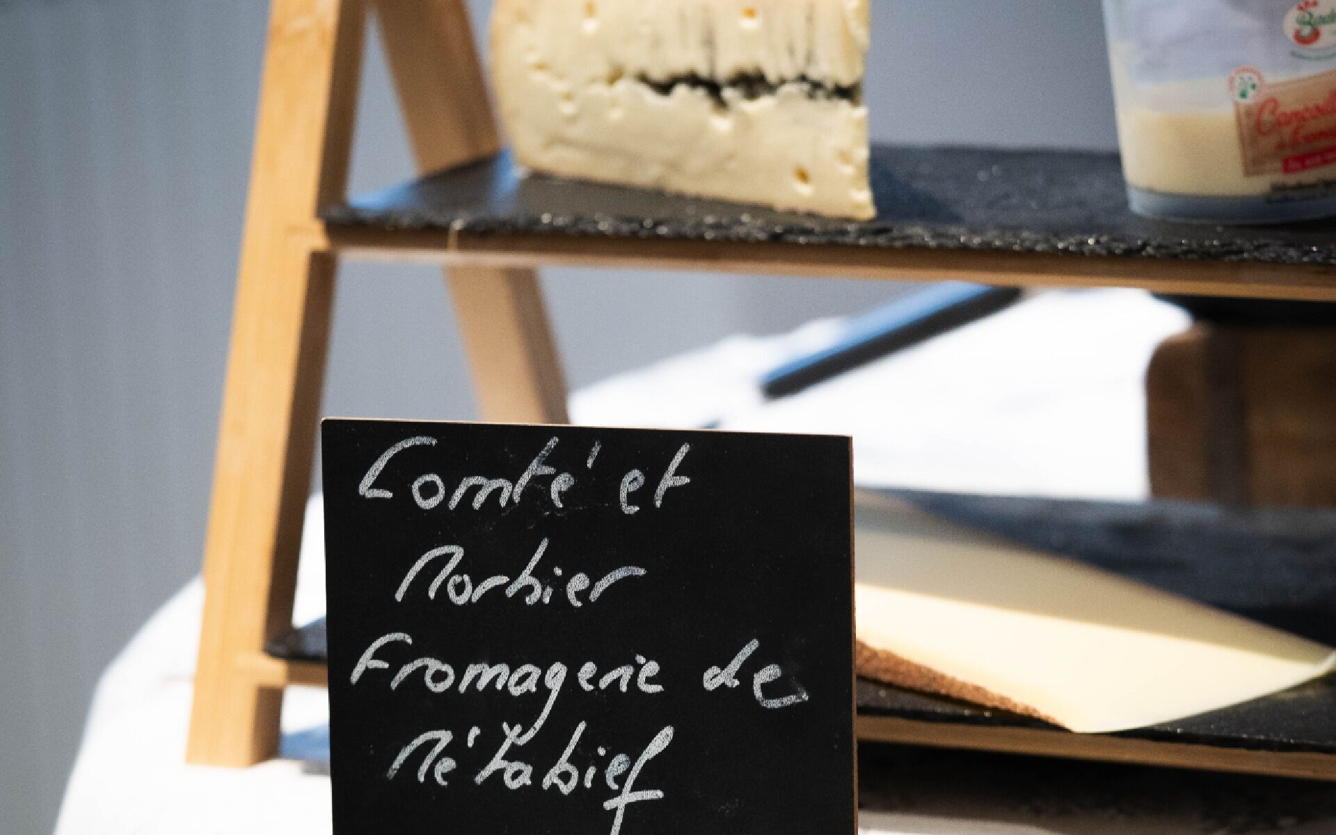 Un cartel de pizarra con el texto 'Comté et Norbier Fromagerie de Neufchâteau' que indica una tienda de quesos.