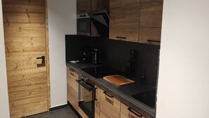 A compact kitchen with wooden cabinets, a black countertop, and modern appliances including a stove, oven, and microwave. - Luxury residence in Métabief, suites, apartments, private spa and sauna (METABIEF)