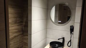A modern bathroom with a wooden shower enclosure, a round mirror, and a black sink with a handheld showerhead.