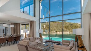 A spacious living area with a large glass wall overlooking a pool and a scenic hillside. - Villa Vigora - Private villa with pool in Korcula (Uvala Vrbovica)
