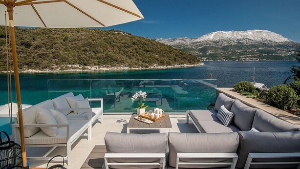 A luxurious outdoor seating area with a glass-bottomed infinity pool overlooking a clear blue sea and a snow-capped mountain. - Villa Vigora - Private villa with pool in Korcula (Uvala Vrbovica)