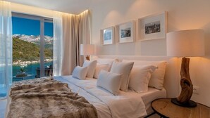 A modern hotel room with a large bed, a view of a coastal landscape, and framed pictures on the wall. - Villa Vigora - Private villa with pool in Korcula (Uvala Vrbovica)