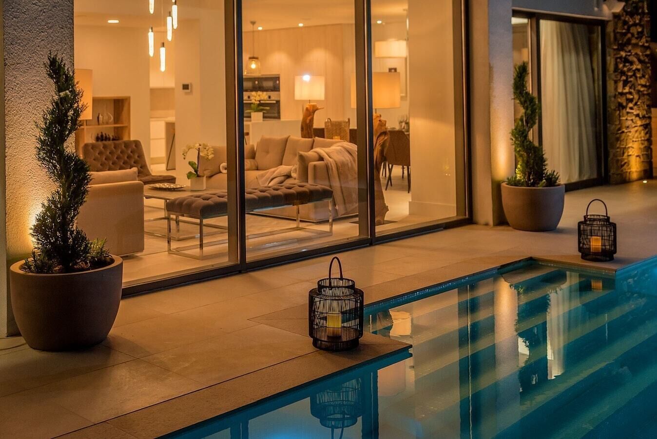 Una hall d'albergo moderna con un'area salotto vetrata, una piscina e piante in vaso.