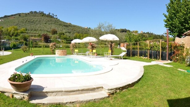 Une piscine rectangulaire bordée d’une terrasse en pierre, entourée d’une pelouse verdoyante et agrémentée de quelques plantes en pot.