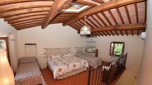 Une chambre avec un grand lit, un plus petit lit, une table de chevet, une lampe, un luminaire suspendu, une fenêtre et un escalier.