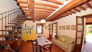 Un intérieur chaleureux avec un escalier en bois, un coin repas avec une table et des chaises, un buffet jaune et un canapé.