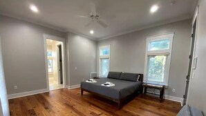 A spacious bedroom with hardwood floors, a large bed, a gray sofa, and a ceiling fan. - PRIVATE ISLAND - 110 Acres in SC (Okatie)