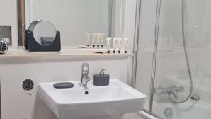 A modern bathroom with a white sink, a toilet, a glass shower enclosure, and a black and white checkered rug. - Immaculate 1-bed Apartment in Milton Keynes (Milton Keynes)