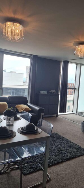 Uma sala de estar moderna com mesa de jantar, sofá de couro preto e uma grande janela com cortinas.