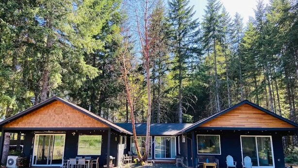 Two cabins with large windows, a deck, and a forest backdrop. - Forest Hideaway House with hot tub and trail (Shelton)