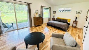 A spacious bedroom with a large bed, a sofa, a small table, and a view of the outdoors through a sliding glass door. - Forest Hideaway House with hot tub and trail (Shelton)