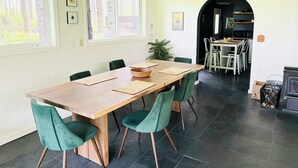 A dining area with a wooden table, green upholstered chairs, and a large window with blinds. - Forest Hideaway House with hot tub and trail (Shelton)