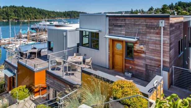 A modern waterfront property with a deck, a wooden door, and a view of boats and water.