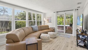 A modern living room with a curved sofa, a small side table, and a large window with blinds.