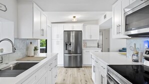 A modern kitchen with white cabinetry, stainless steel appliances, and a wooden floor.