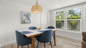 A dining area with a table, chairs, a hanging light fixture, a window with blinds, and a wall-mounted painting.