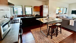 A modern kitchen with a central island, a dining area, and a living room with a sofa and TV. - ✨NEW✨ Bright in-town Penthouse with roof deck 😎 (Friday Harbor)
