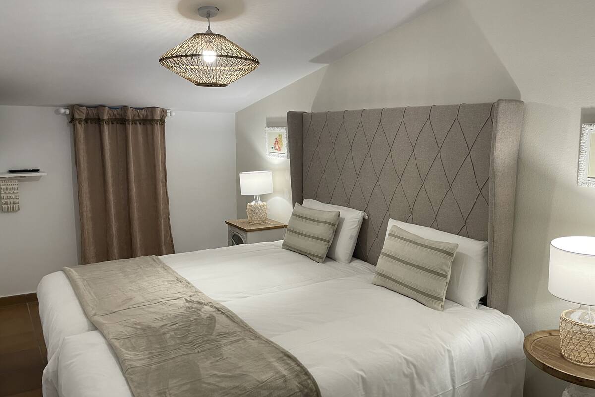 Et pænt indrettet hotelværelse med en stor seng, et natbord med lampe, en dekorativ loftlampe og et vindue med gardiner.