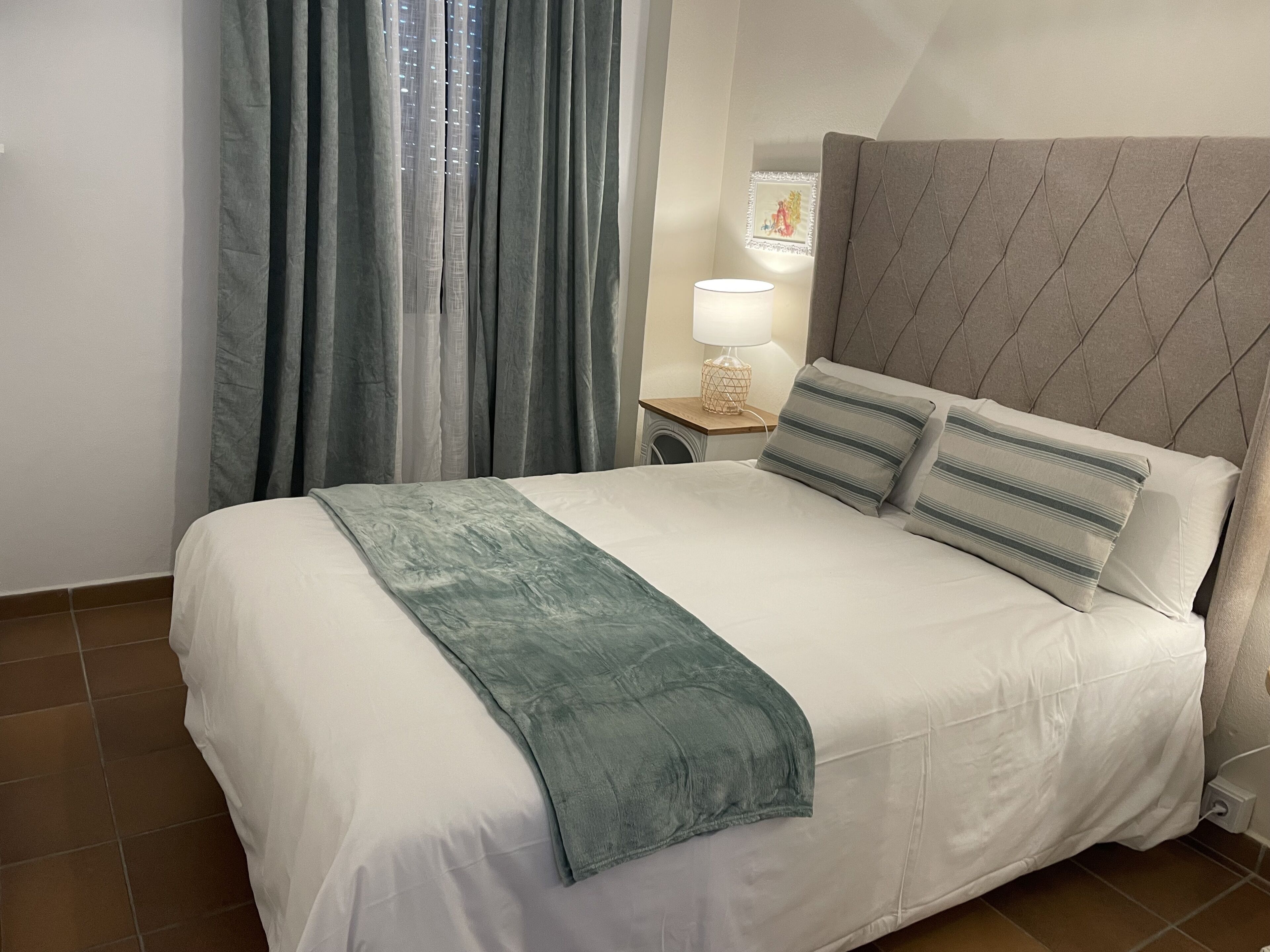 A neatly made bed with a grey headboard, white bedding, and a teal throw blanket.