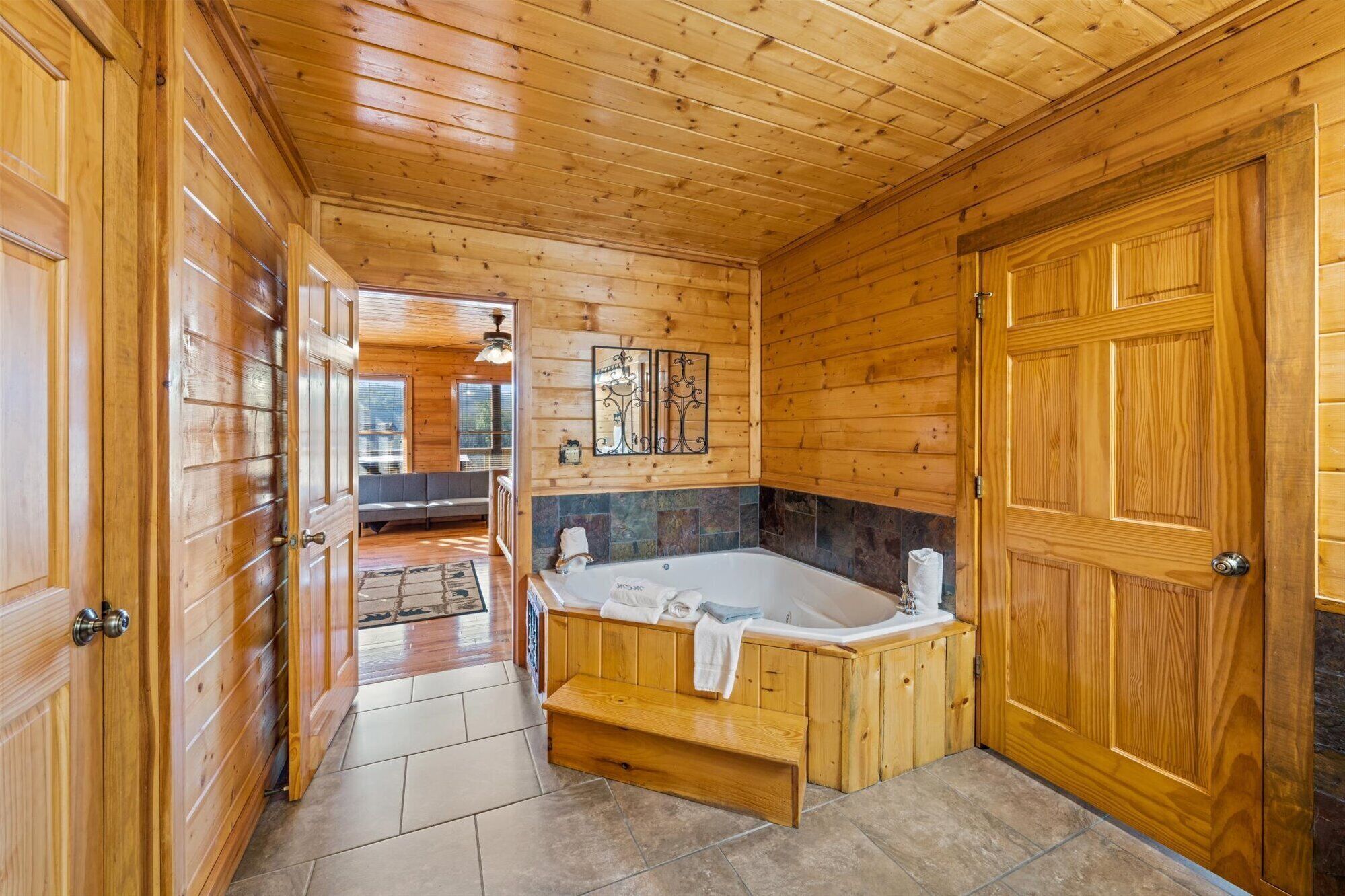 A wooden cabin interior with a bathroom featuring a bathtub, a bench, and a tiled floor.