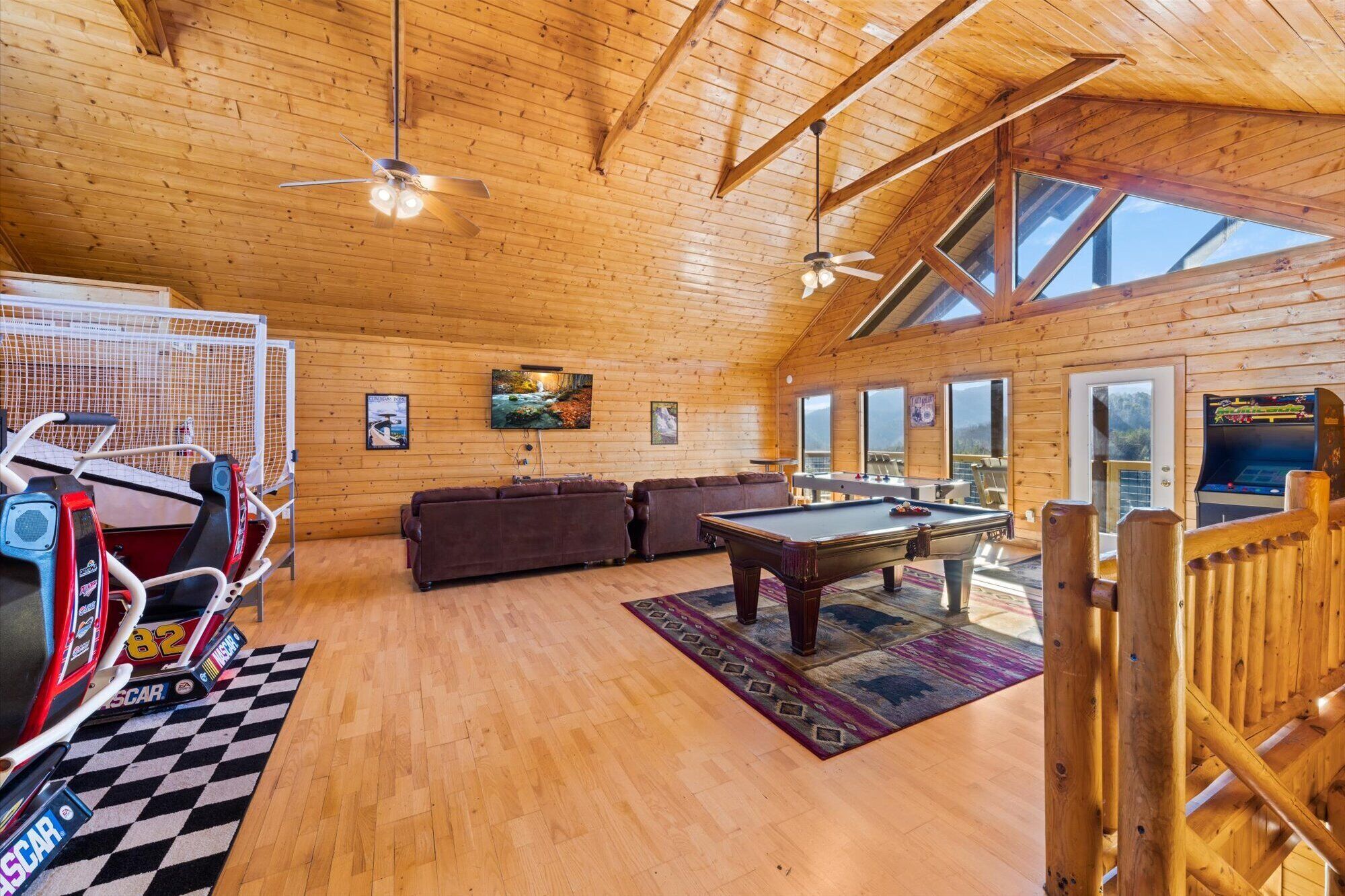 A spacious room with wooden walls and a high ceiling, featuring a pool table, a sofa set, and a NASCAR racing car display.