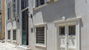 Un edificio con entrada empedrada en piedra, puertas blancas con paneles de vidrio y una puerta verde.