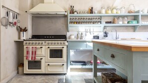 Una cocina con estufa blanca, repisas con frascos y un colgador para utensilios.