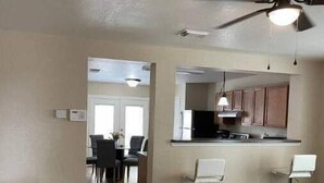 Amplia sala de estar con una mesa de comedor y sillas, una cocina con barra y un ventilador de techo.
