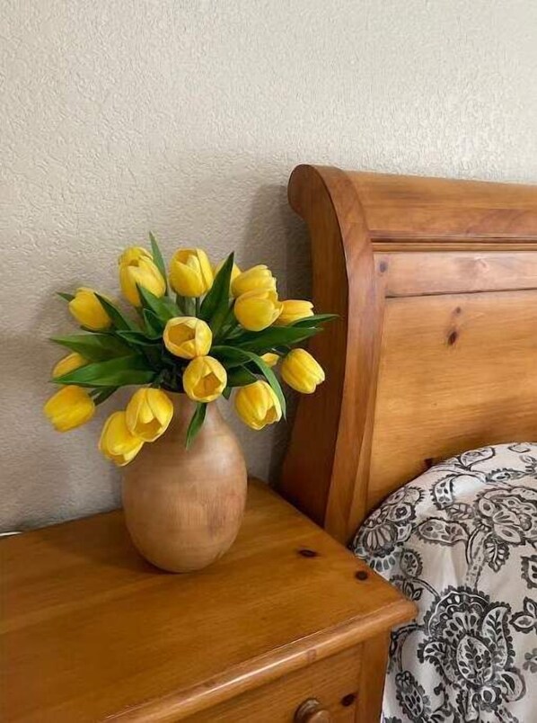 Une table de chevet en bois sur laquelle est posé un vase de tulipes jaunes.