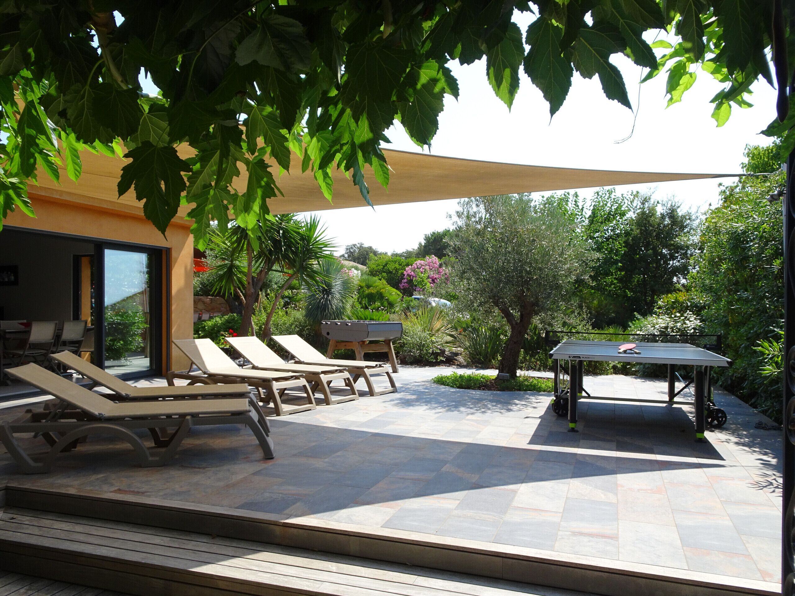 An outdoor patio with sun loungers, a barbecue grill, and a ping pong table.