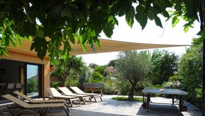 An outdoor patio with sun loungers, a barbecue grill, and a ping pong table.
