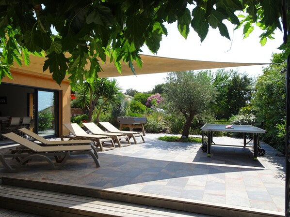 An outdoor patio with sun loungers, a barbecue grill, and a ping pong table.