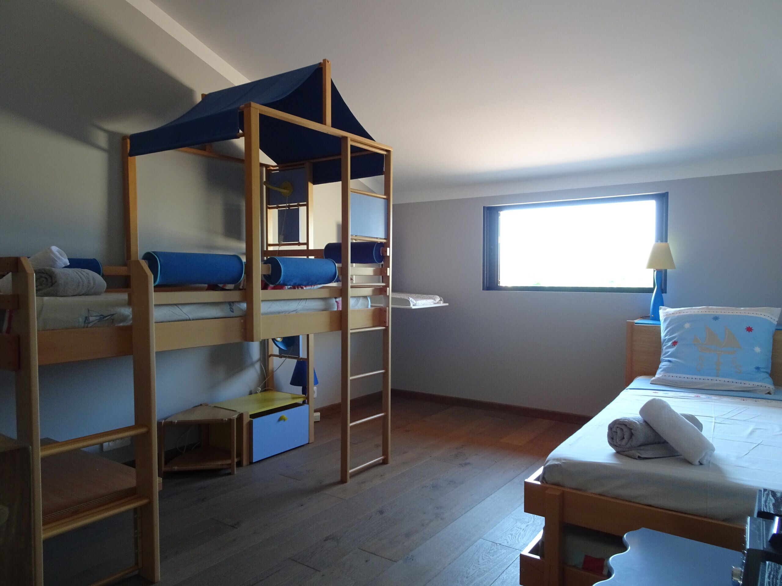 Une chambre de type dortoir, équipée de lits superposés, d’un petit bureau et d’une fenêtre laissant entrer la lumière naturelle.