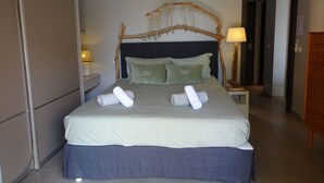 A neatly made bed with a dark headboard, two pillows, and two rolled towels on the bed.