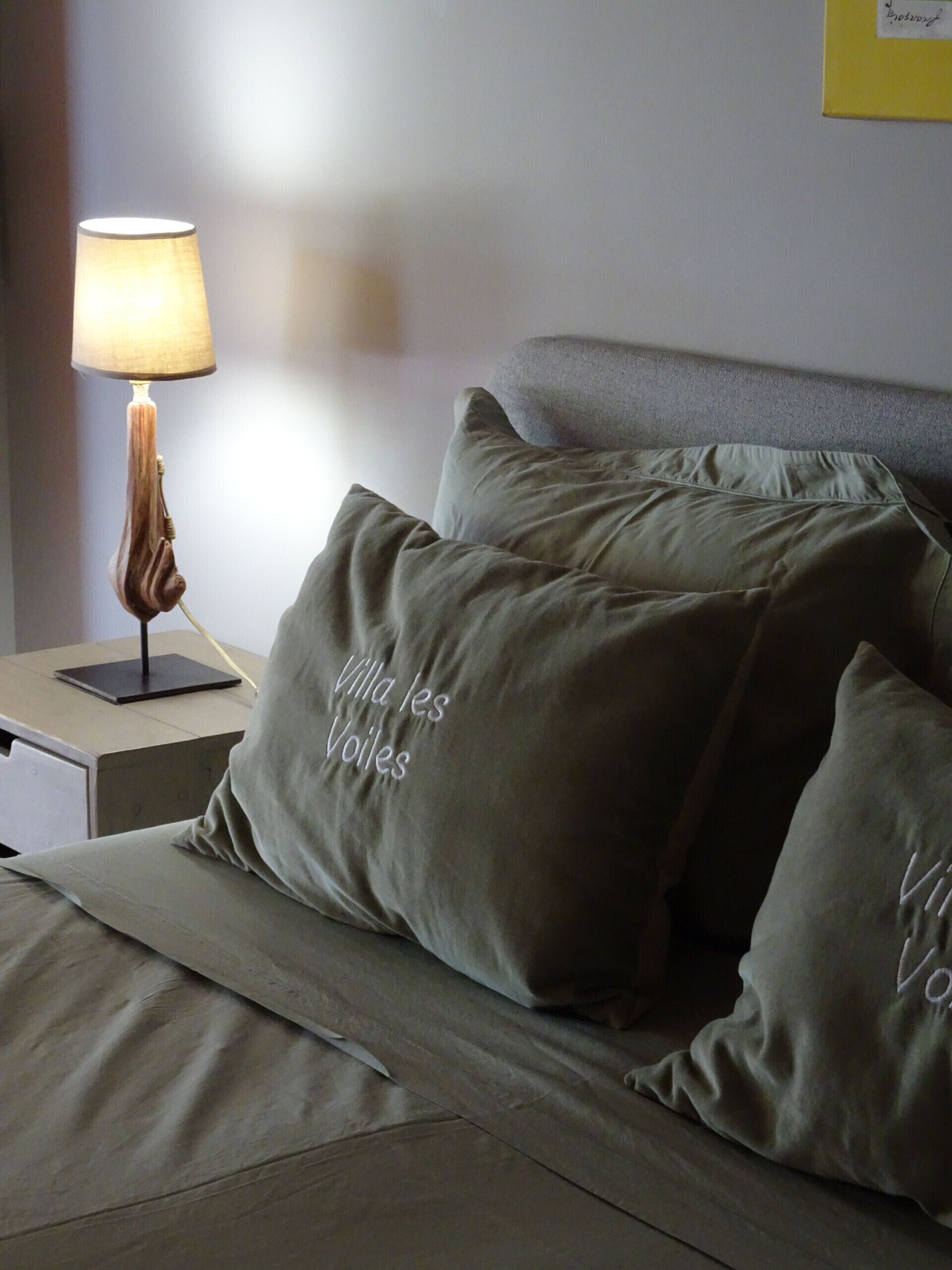Un lit bien fait, avec une literie et des oreillers verts, une table de chevet avec une lampe, et un mur orné d’un tableau encadré.