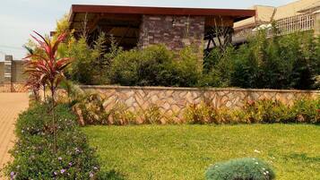 A building with a stone facade, a red roof, and a garden with various plants and flowers.