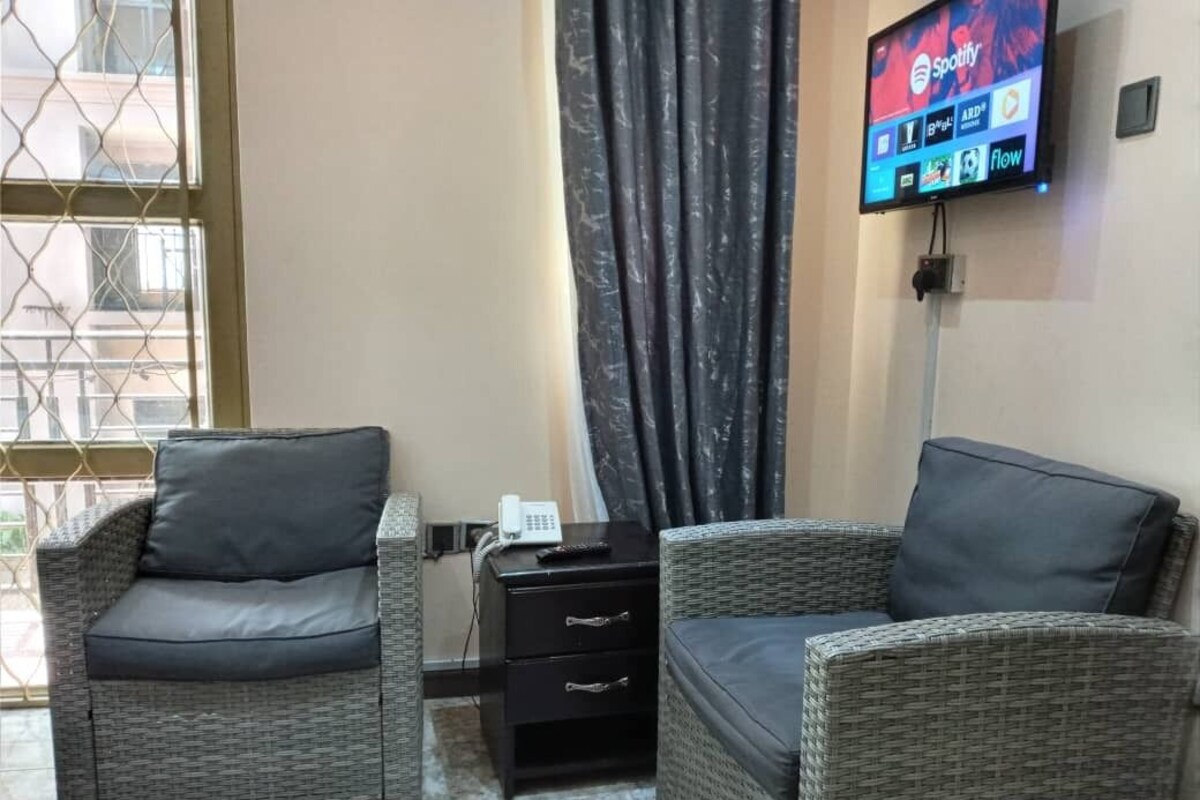 Una habitación con dos sillones de mimbre, una mesita con un teléfono y un televisor mostrando Spotify.