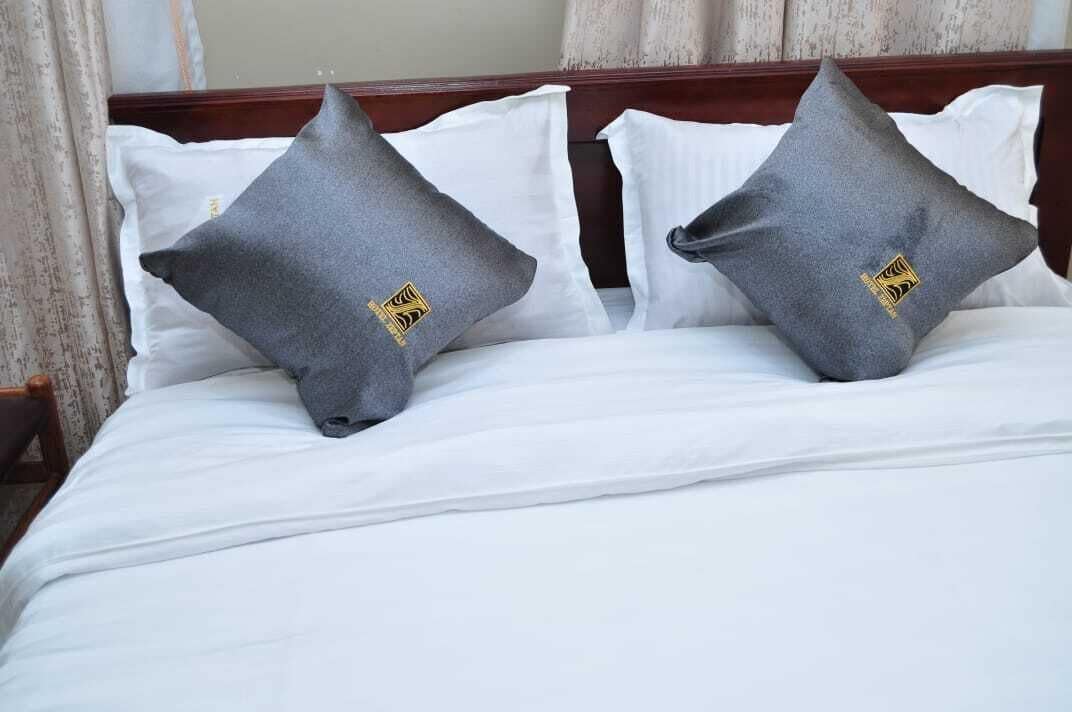 A bed with white bedding and two grey pillows with a logo.