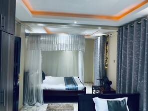 A bedroom with a bed, a bedside table, a chair, and a window with curtains. - Hotel Zeptan (Jinja)
