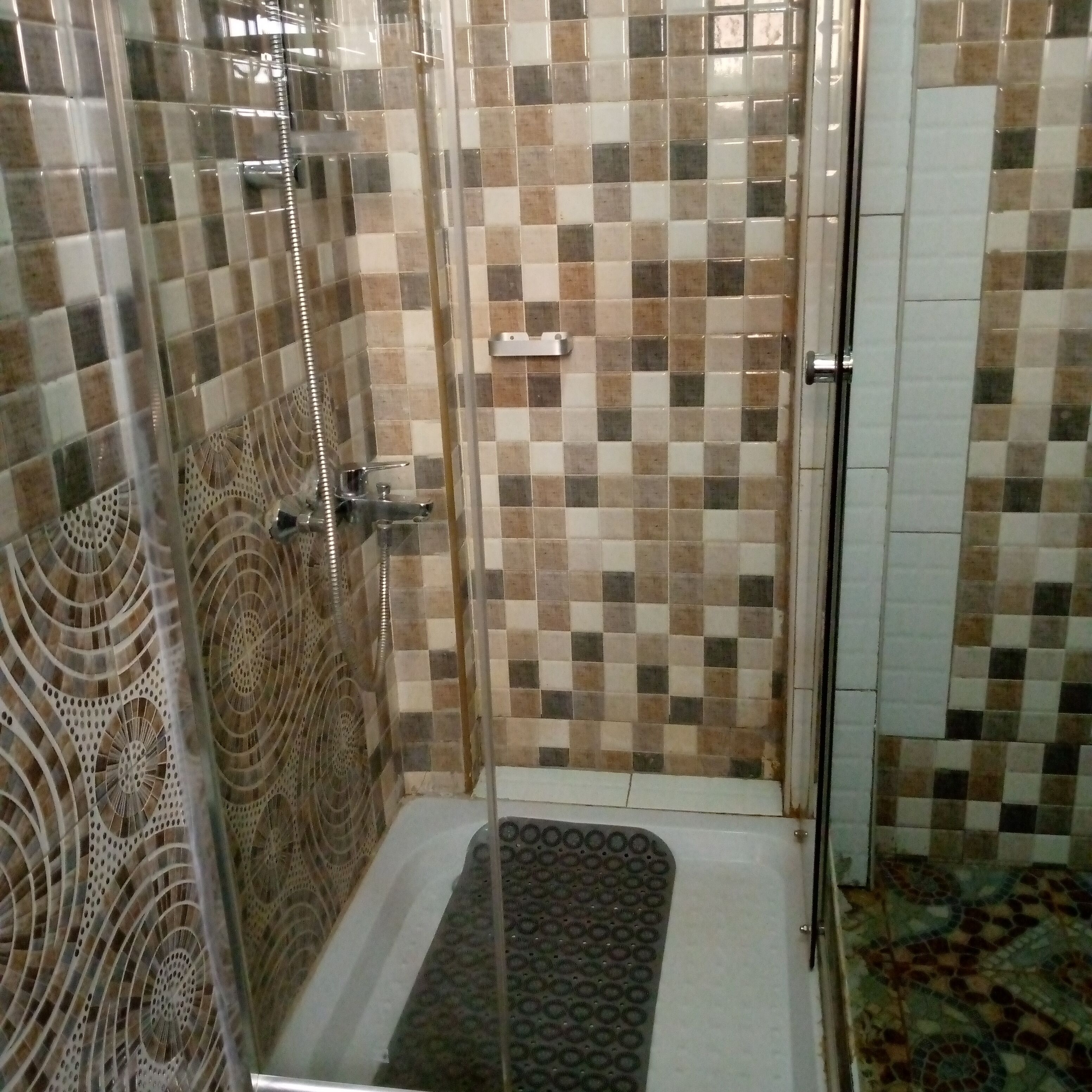 A shower area with checkered tile walls, a glass door, and a patterned mat.