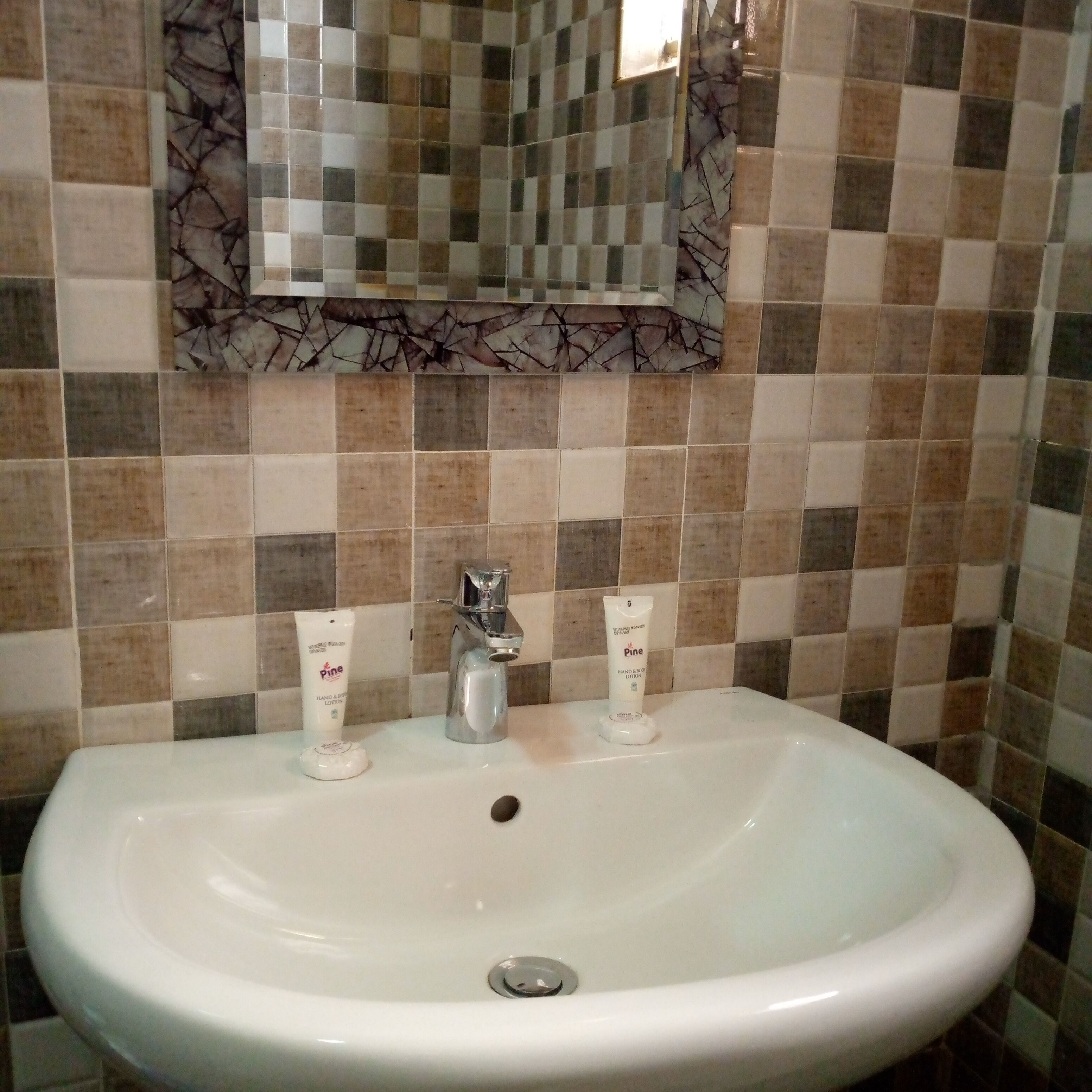 Un baño con un lavabo blanco, dos dispensadores de loción para manos y cuerpo, un espejo y una pared con azulejos.
