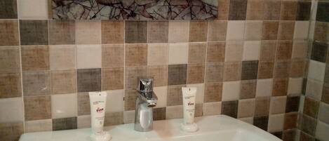 A bathroom with a white sink, two hand and body lotion dispensers, a mirror, and a tiled wall.