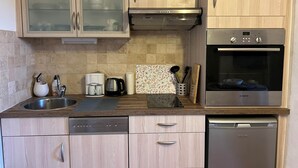 A modern kitchen with wooden cabinets, a Bosch oven, a dishwasher, and a coffee maker. - Gîte 2 Personnes Bruyère - 35 m² (Niozelles)