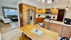 A modern kitchen with wooden cabinets, a stainless steel refrigerator, a microwave, and a stove. There is a dining area with a wooden table and chairs. - Comfortable 3BR Home-Prime Video, WiFi, Parking (Schererville)
