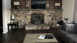 Un salon avec une cheminée en pierre, un téléviseur à écran plat fixé au-dessus, un canapé et une table basse.