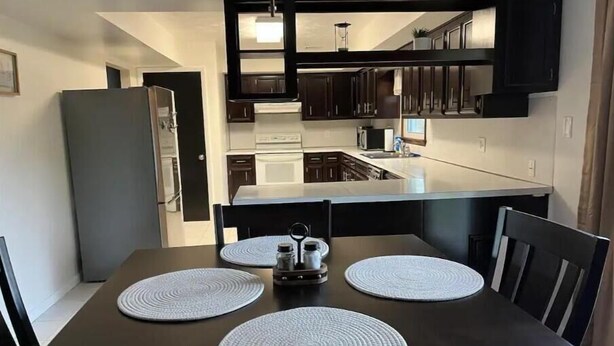 Une cuisine moderne avec des meubles de couleur sombre, un îlot central et une table à manger agrémentée de sets de table.