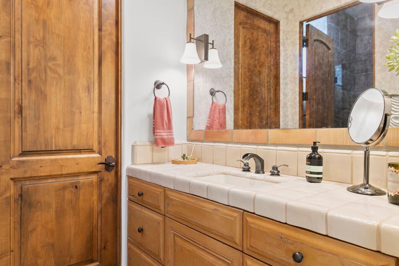 A bathroom with wooden cabinetry, a white countertop, a sink with a single faucet, a mirror, and a towel rack with two towels.