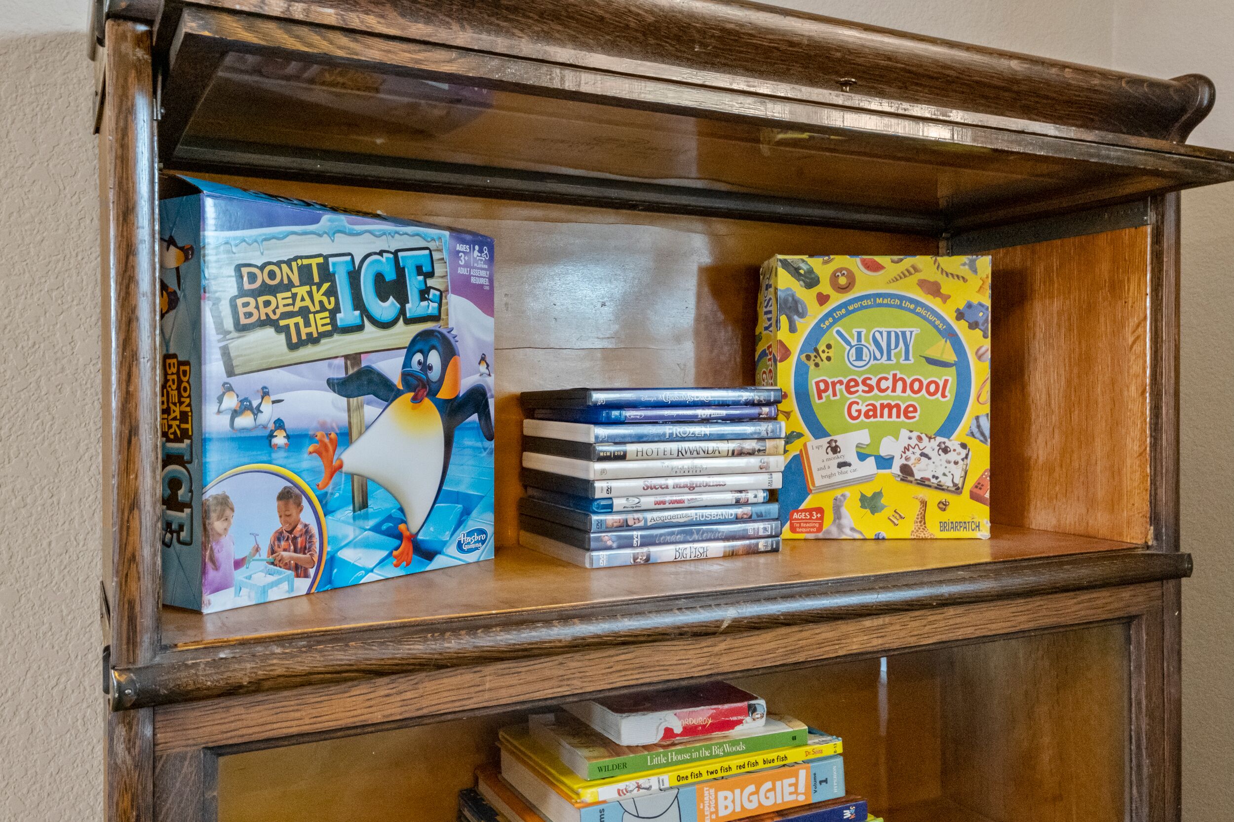 A wooden shelf with a collection of board games, including 'Don't Break the Ice' and 'Spy Preschool Game'.